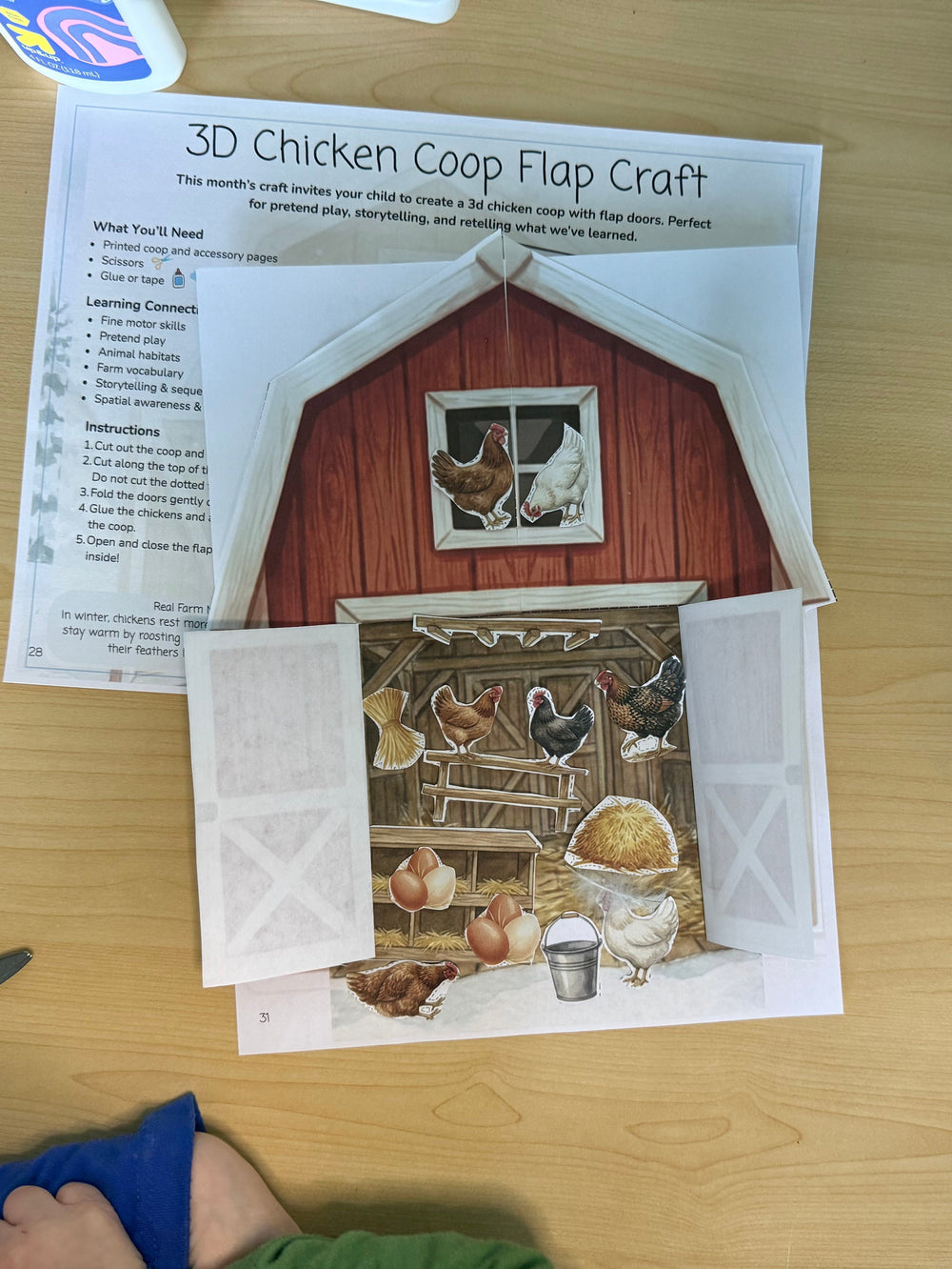 3D chicken coop flap craft on a table with scissors and glue.
