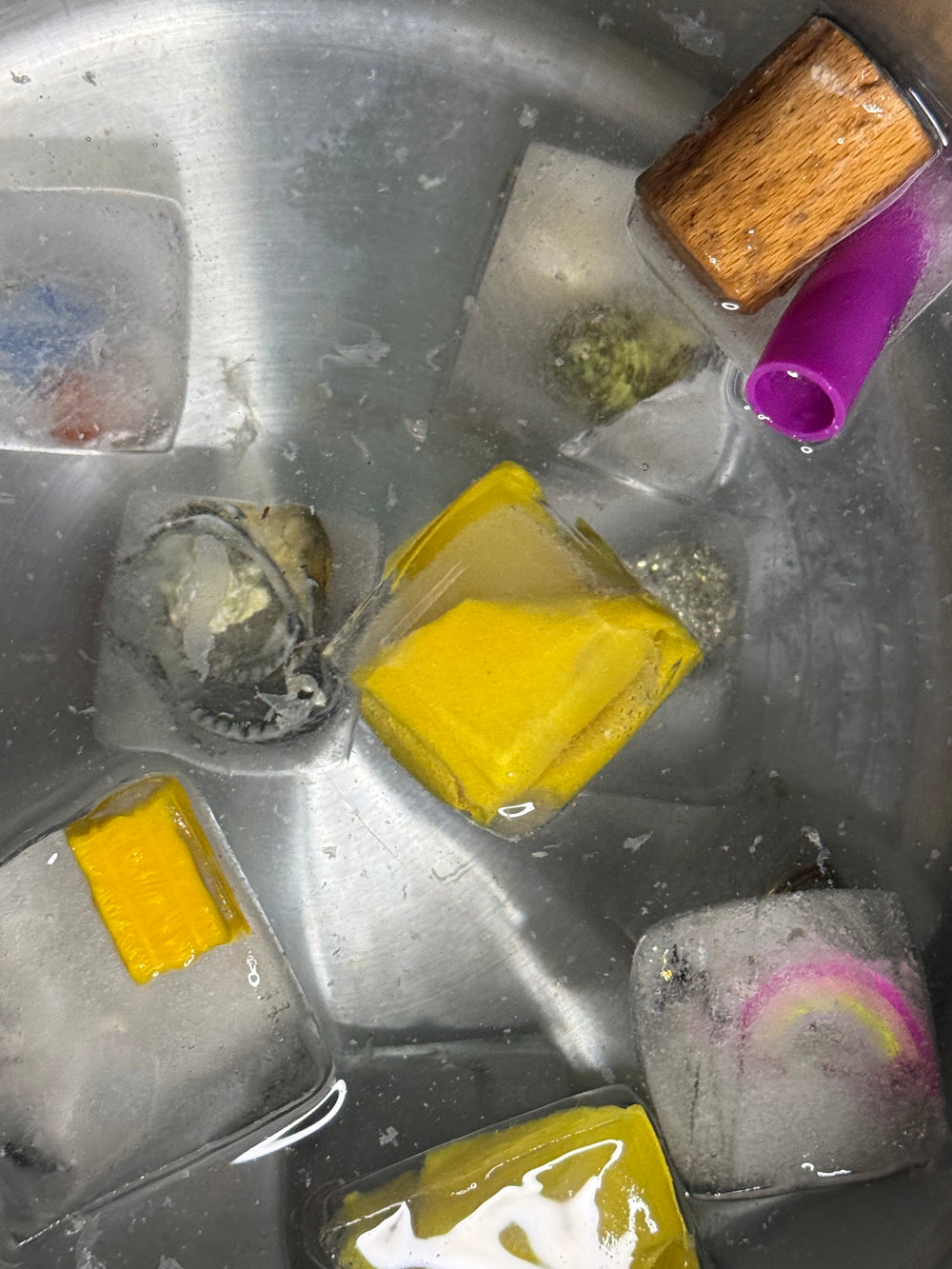 Ice cubes with various colorful objects inside a metal container